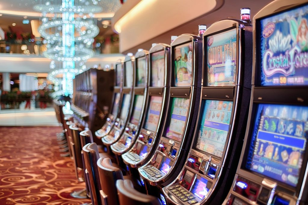 A row of illuminated slot machines receding down a casino aisle.