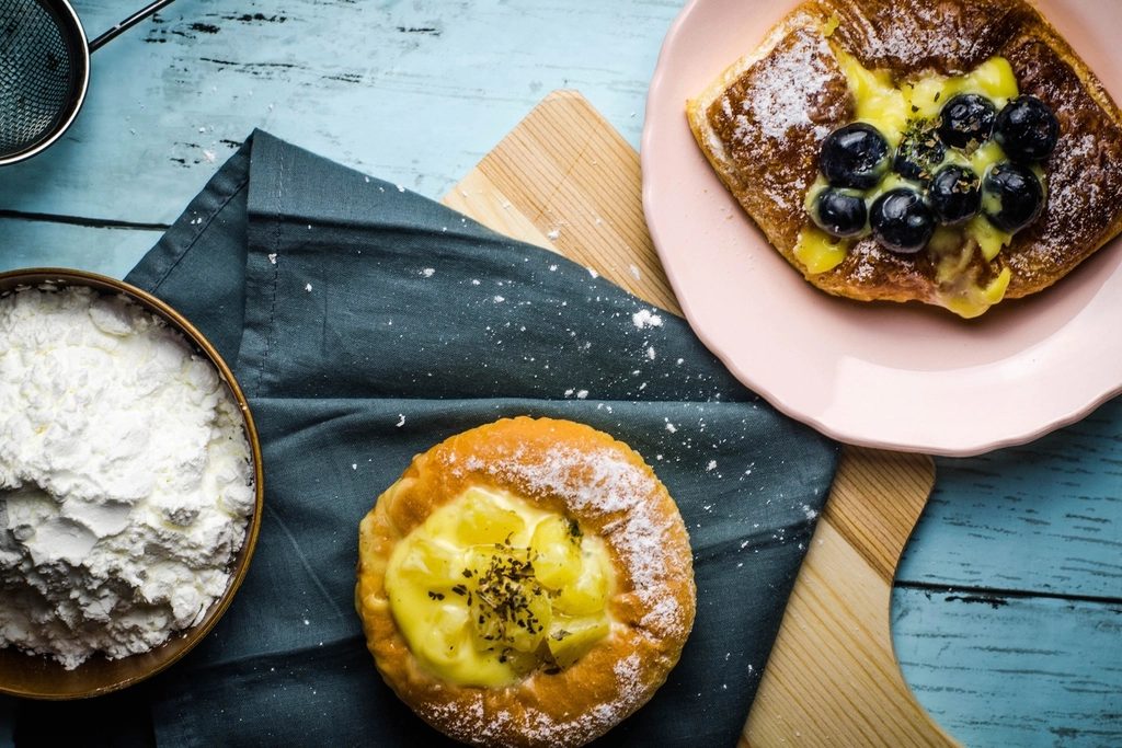 Pastries topped with blueberries and cream on ceramic plates beside a dish of flour.