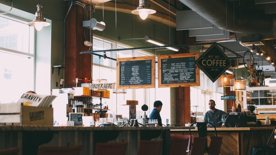The interior of a casual café with a long service counter, bar stools and a chalkboard menu.