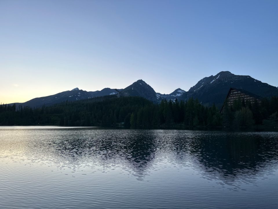 A still lake at dusk reflecting a ridge of dark mountains and a pale sky.