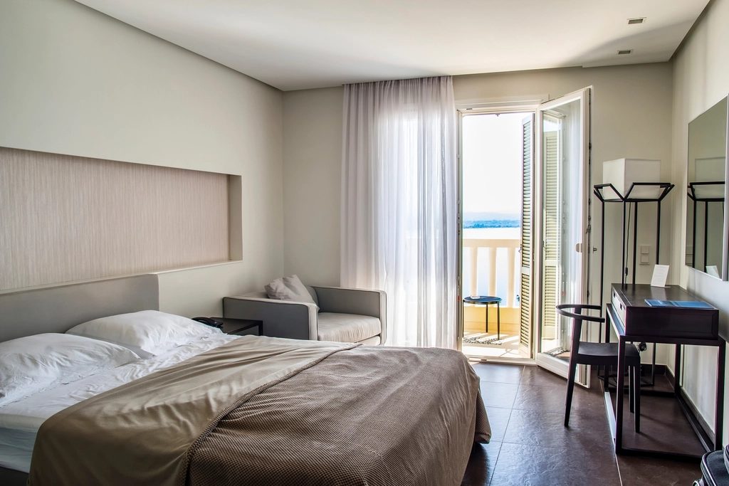 A hotel bedroom with two beds side by side, pale linen and a glazed door onto a balcony.