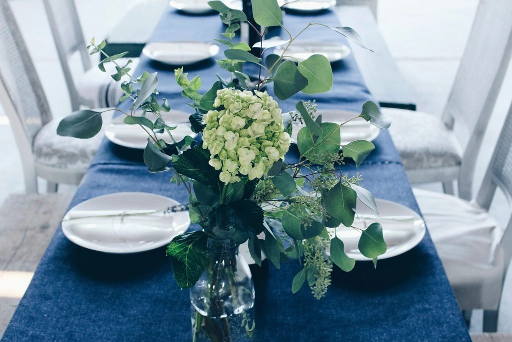 A banquet table laid with white china, blue runners and low arrangements of white flowers.